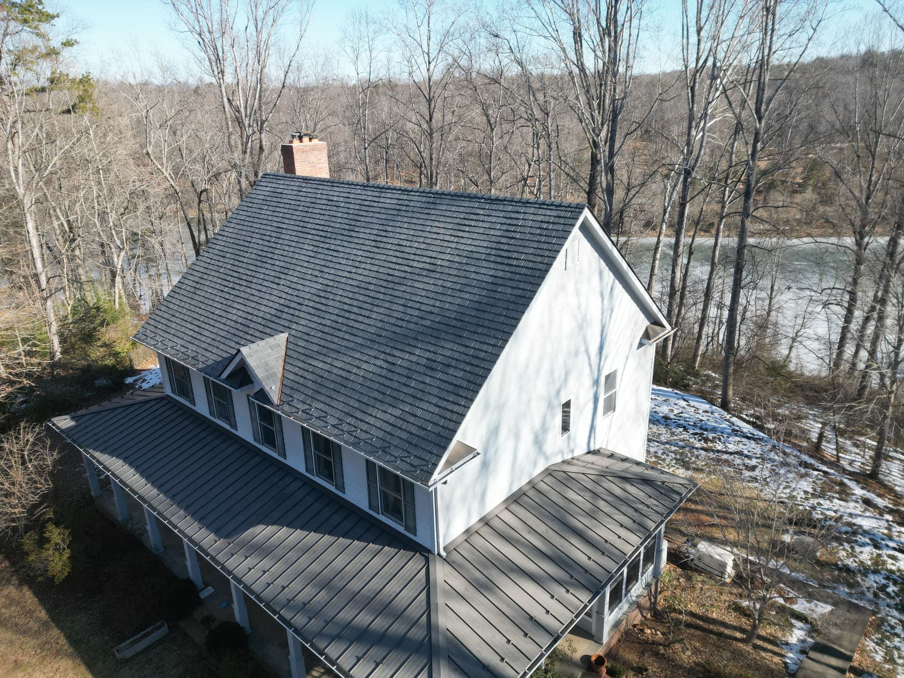 Aerial view of a Lake Monticello home with a new asphalt and metal roof by Lounsbury Roofing, lake visible in the background