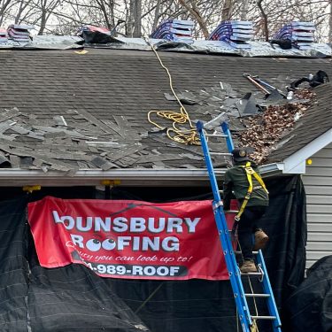 Charlottesville roof repair in progress. Man scales a ladder adjacent a Lounsbury Roofing banner